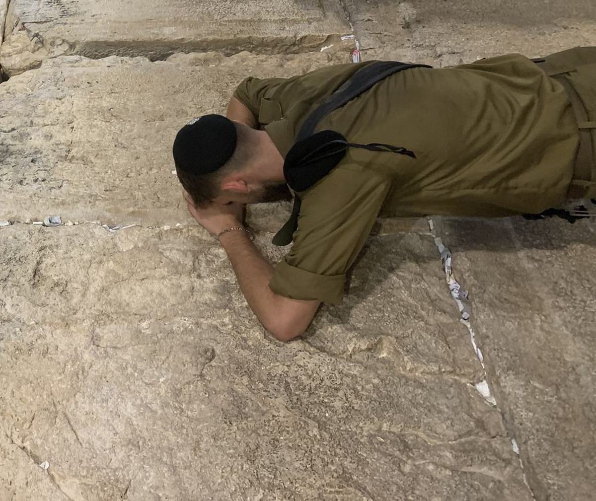 A young soldier with his forehead pressed against the stone of the Western Wall.
