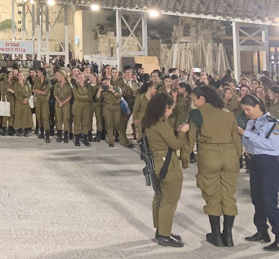 Young women soldiers with rifles standing together in the plaza at night.